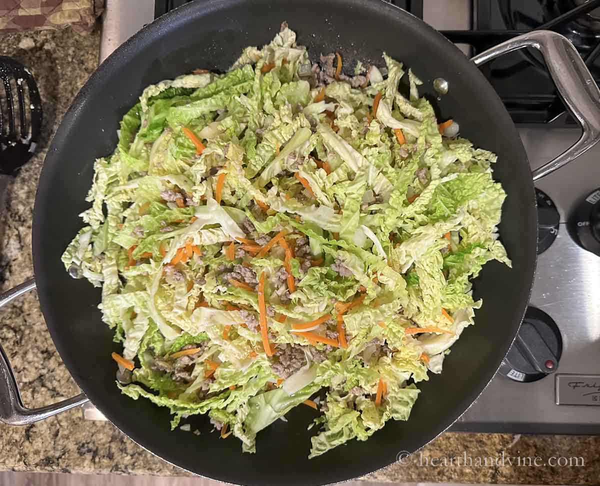 Ground pork, shredded cabbage, and carrot sticks in a skillet on the stove.