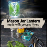 Lit mason jar fern lantern over supplies including wire, ferns, glue and more.