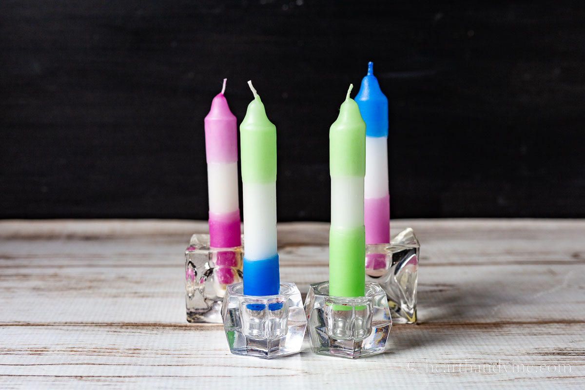 Four colorful dip dyed candles set in small candlesticks.