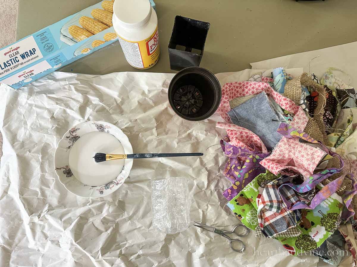 Supplies to make fabric bowls including mod podge, scrap fabric, plastic wrap, small pots and a paintbrush.