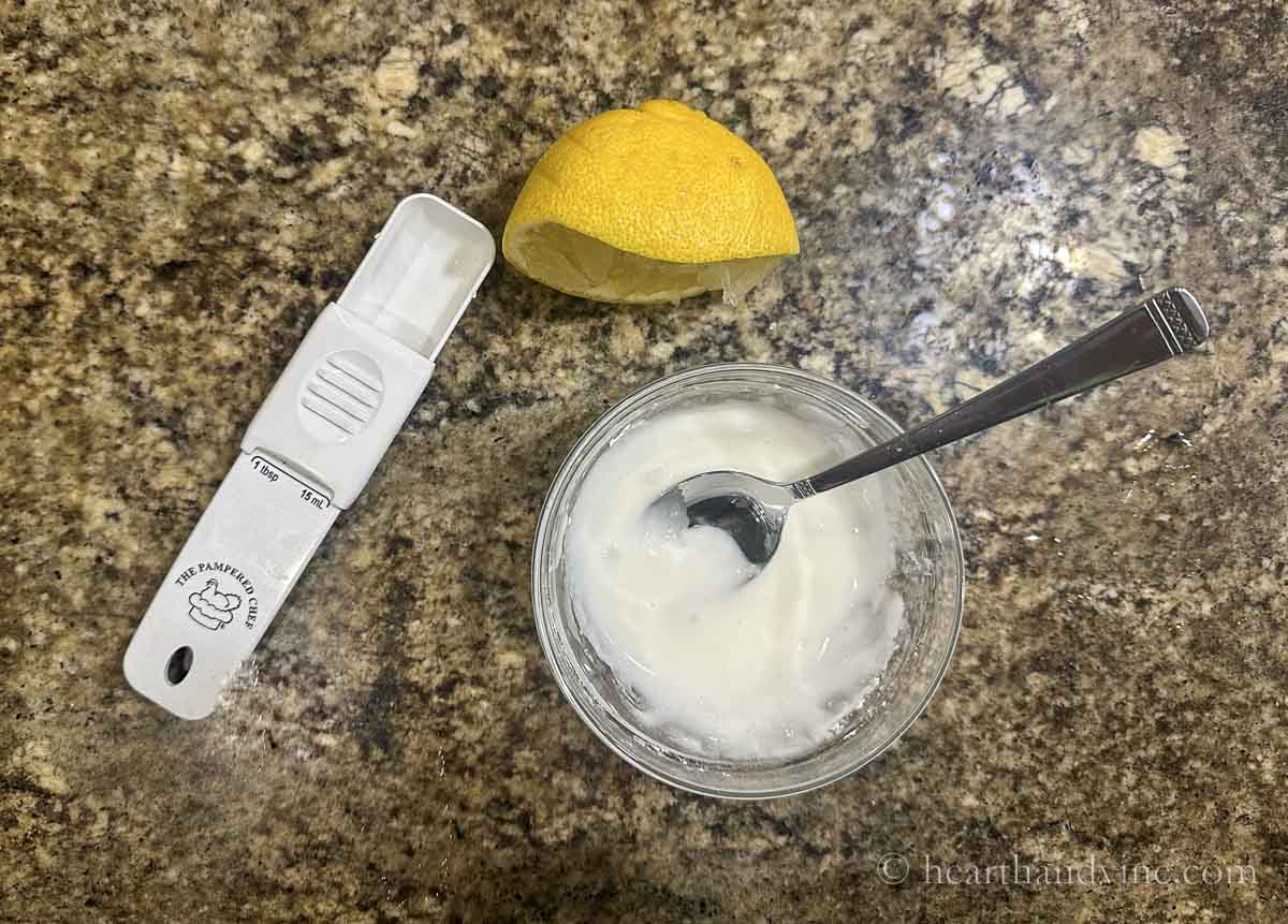 Small bowl of lemon glaze with a spoon. A half of a lemon and a measuring spoon.