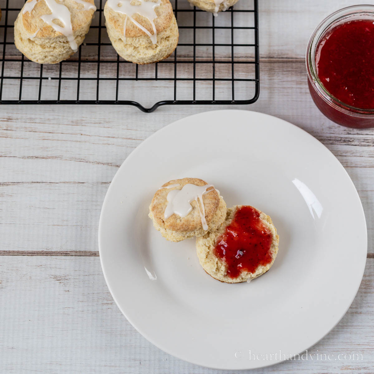 A glazed scone pulled apart with a dollop of strawberry jam on the bottom half.
