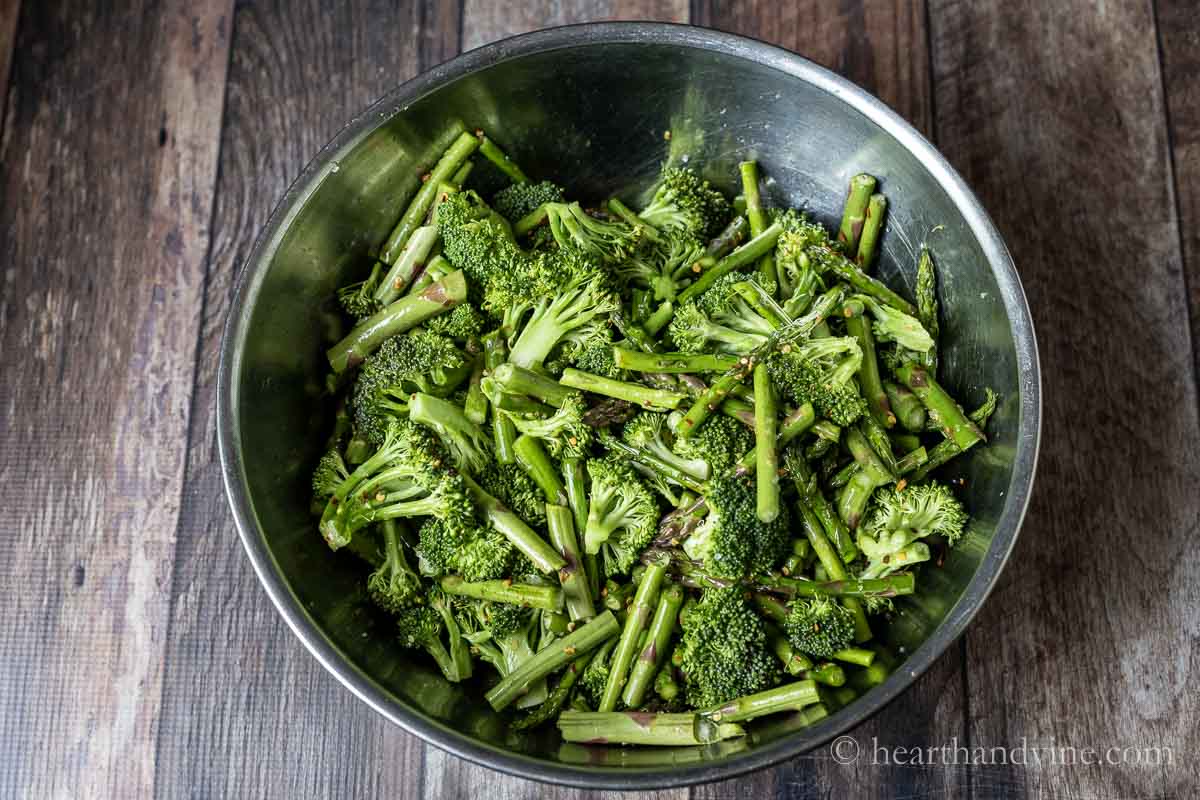 Broccoli and asparagus tossed with olive oil and spices in a large bowl.