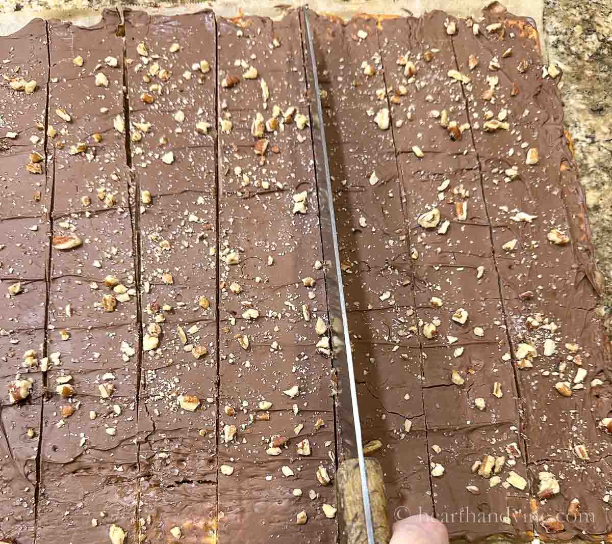 A large knife scoring and cutting the pretzel toffee.