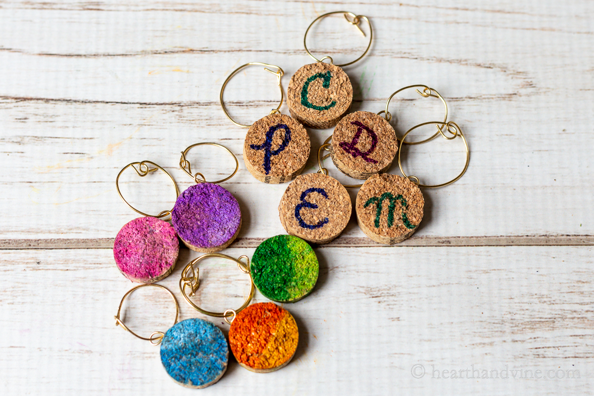 A group of wine charms made from slices of wine cork and wire clasps. Some are different colors and some have black letters.
