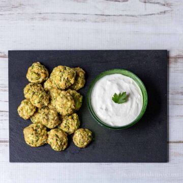 Baked zucchini bite on a slated tray with a bowl of horseradish sauce.