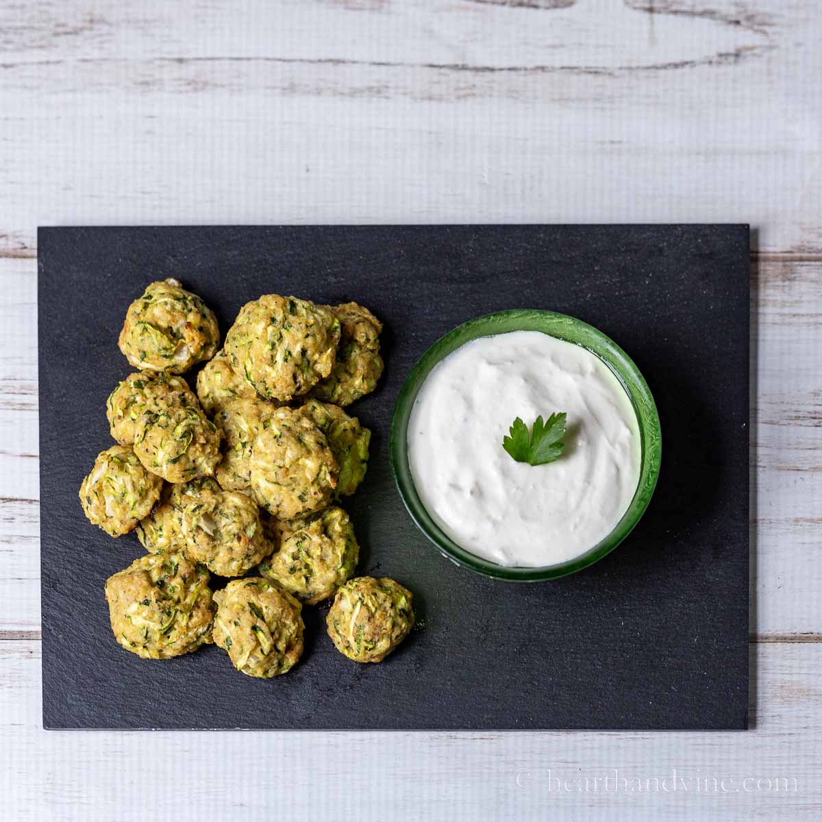 Baked zucchini bite on a slated tray with a bowl of horseradish sauce.
