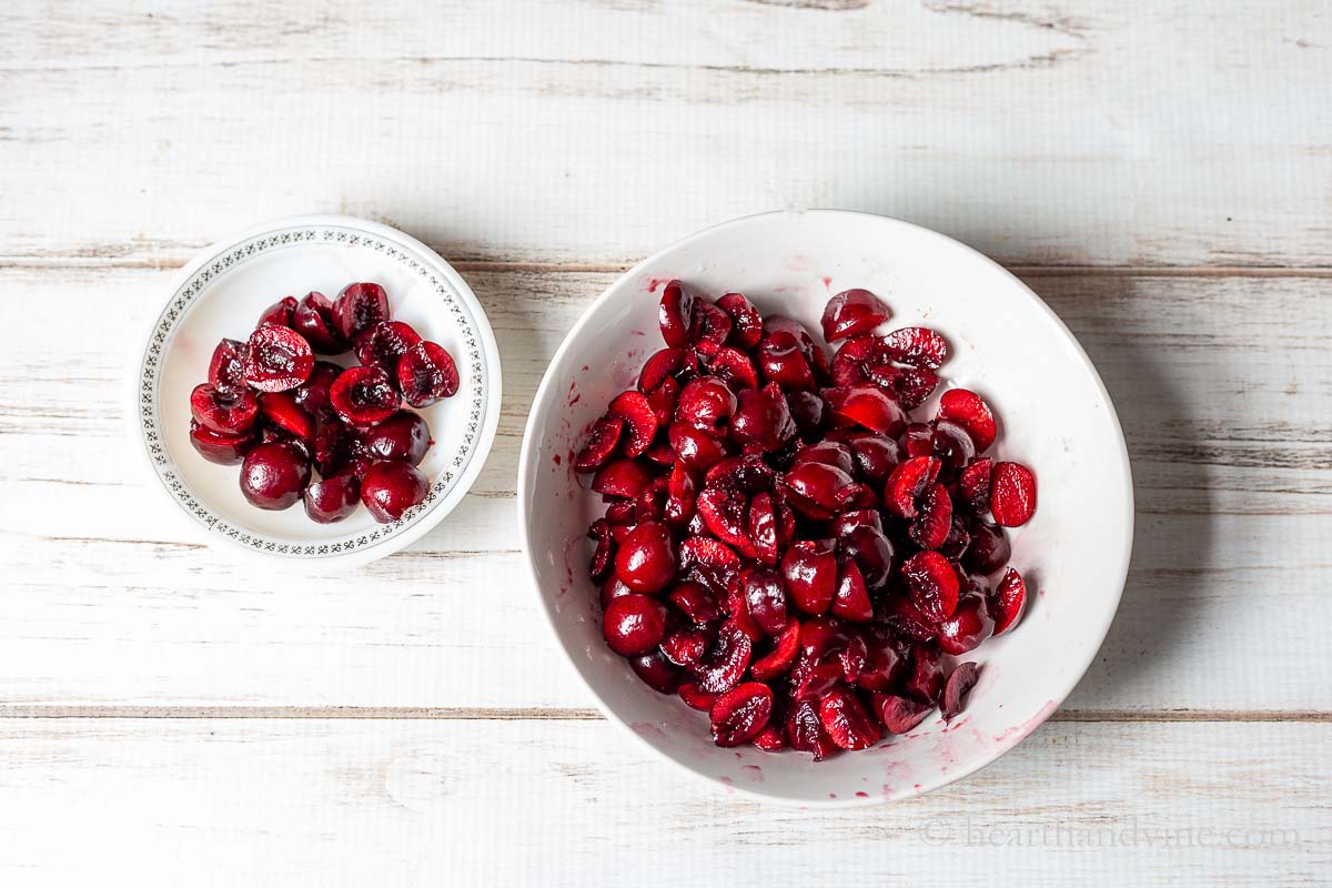 A small bowl with halved black cherries and a larger one with chopped black cherries.