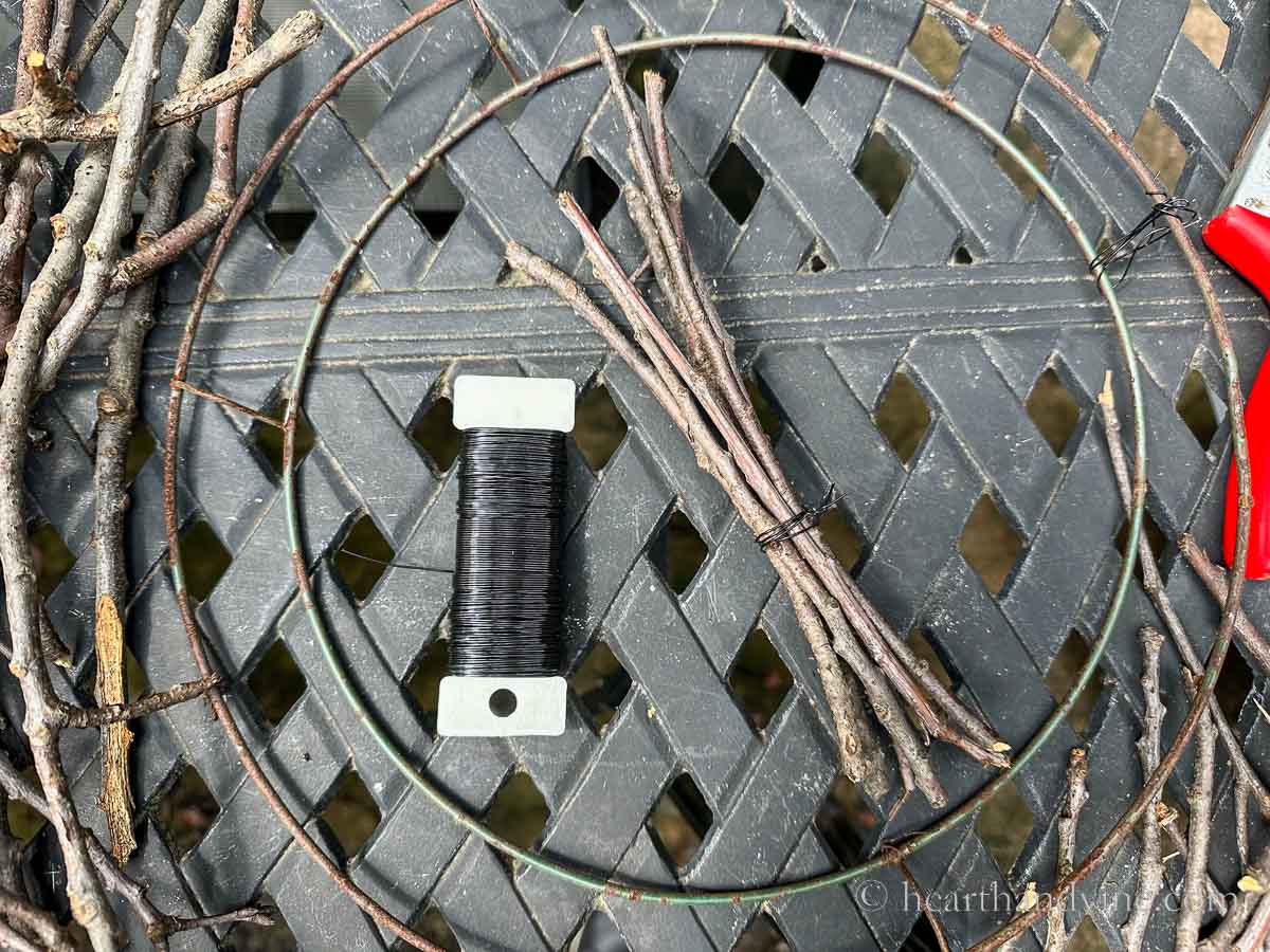 A bundle of twigs wrapped together with black floral wire next to a paddle of wire.