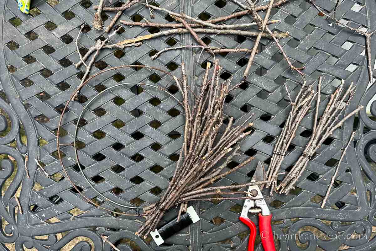 More bundles of twigs wired onto a wreath frame with a pair of pruners and a floral wire paddle in black.