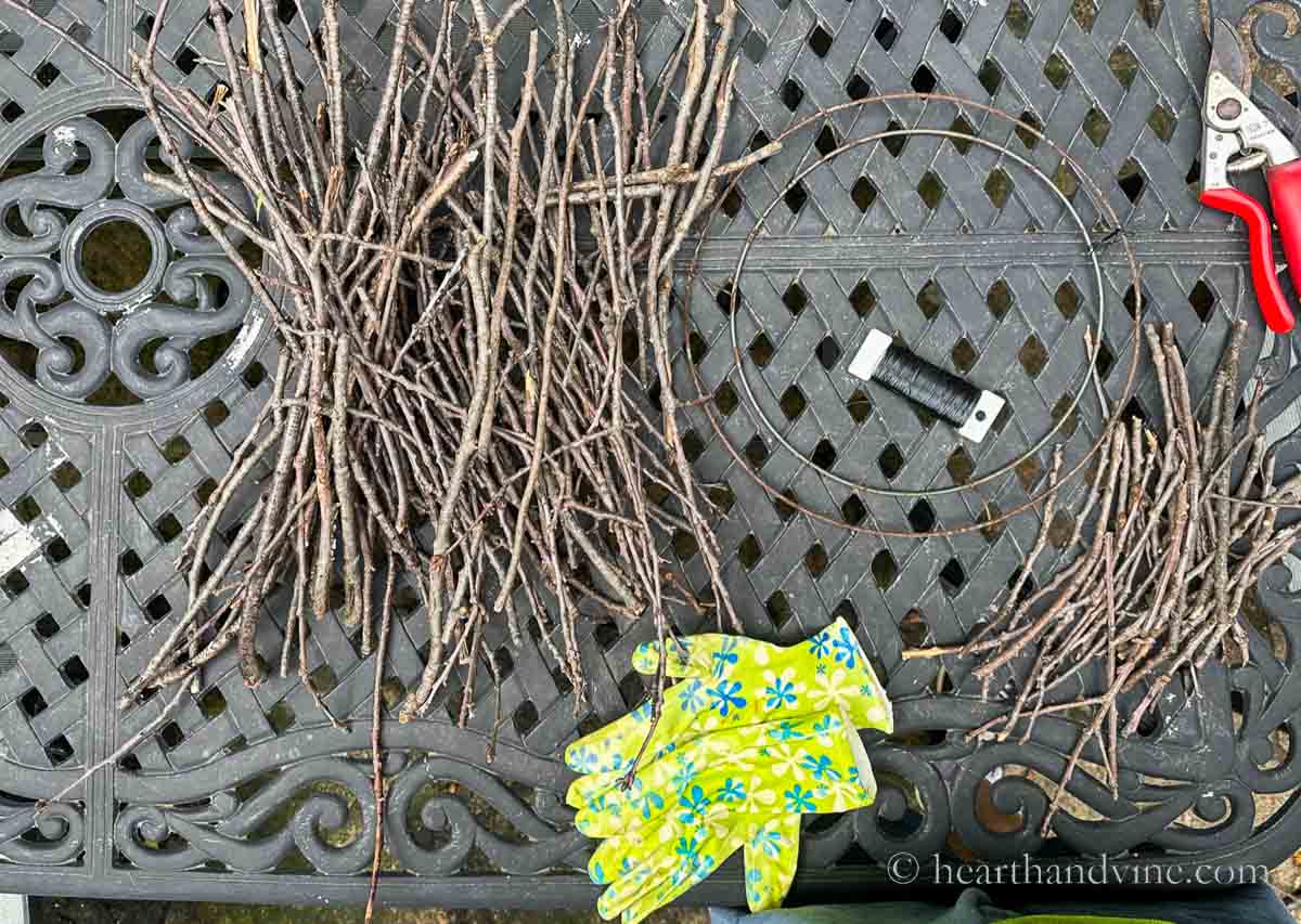 Supplies for making a twig wreath including collected twigs or branches, floral wire in black and pruners.