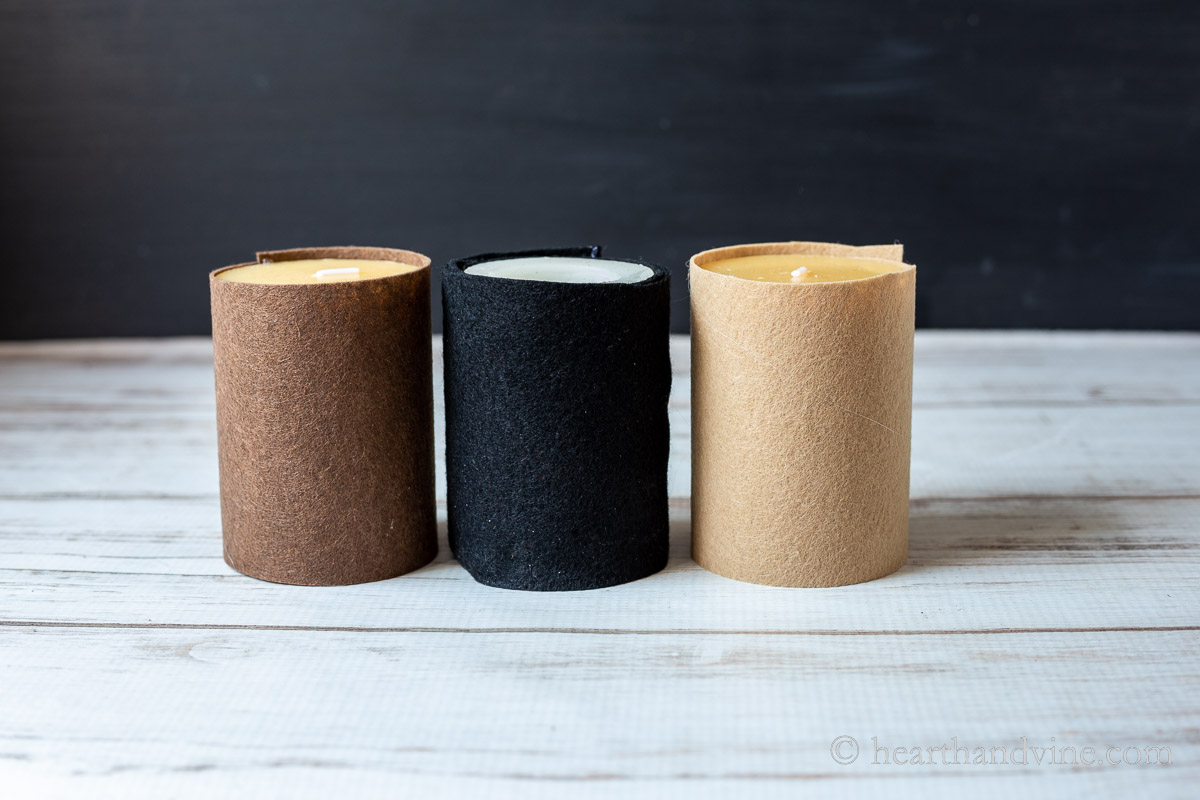 Three pillar candles covered with felt in tan, black and brown.