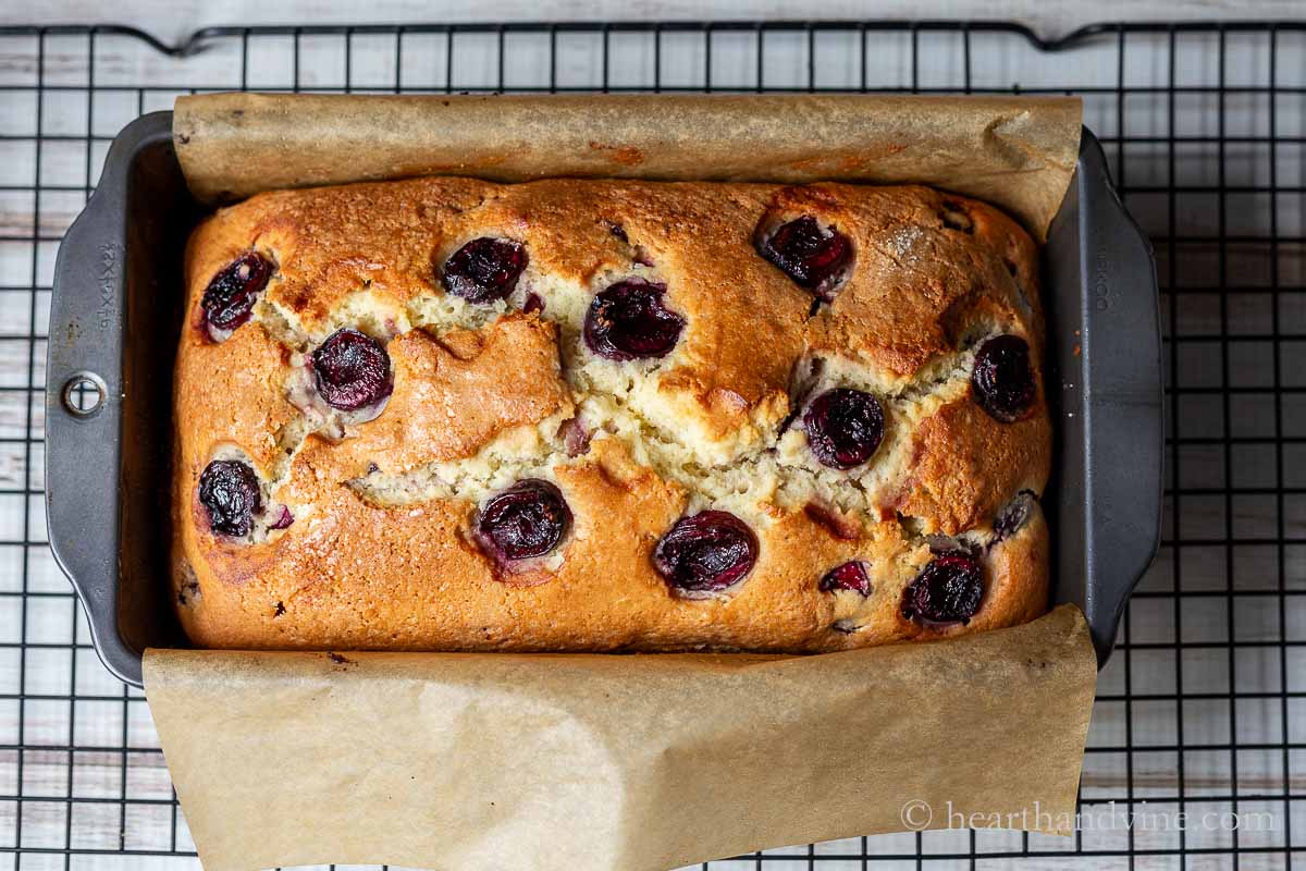Cherry cake in a loaf pan fresh from the oven on a cooling rack.