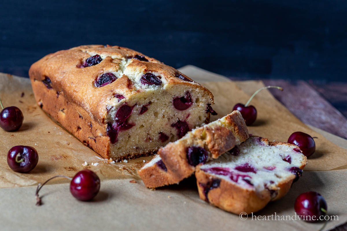 Cherry cake out of the loaf pan with a few slices and fresh cherries around the cake.
