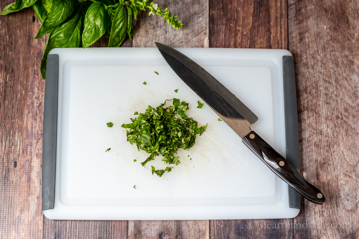 Fresh chopped basil and a chef knife on a cutting board.