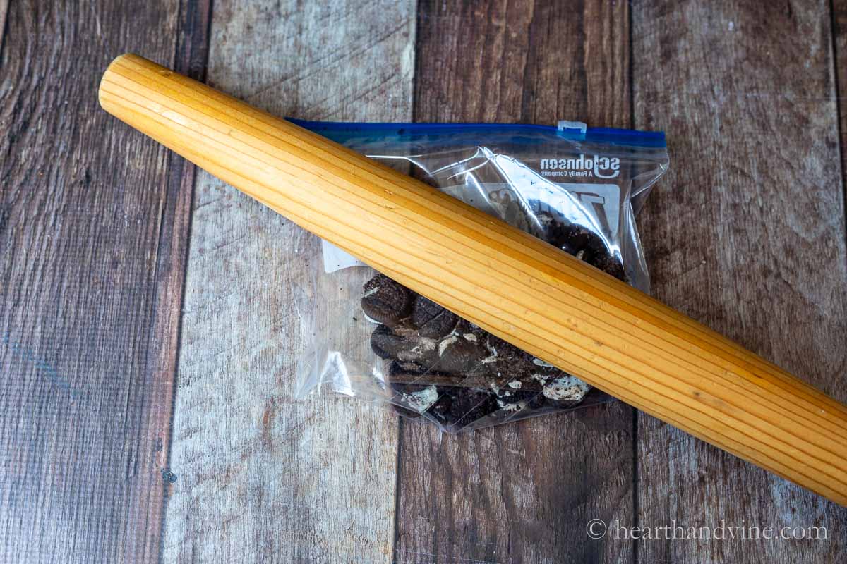 A rolling pin crushing Oreo cookies in a plastic bag.