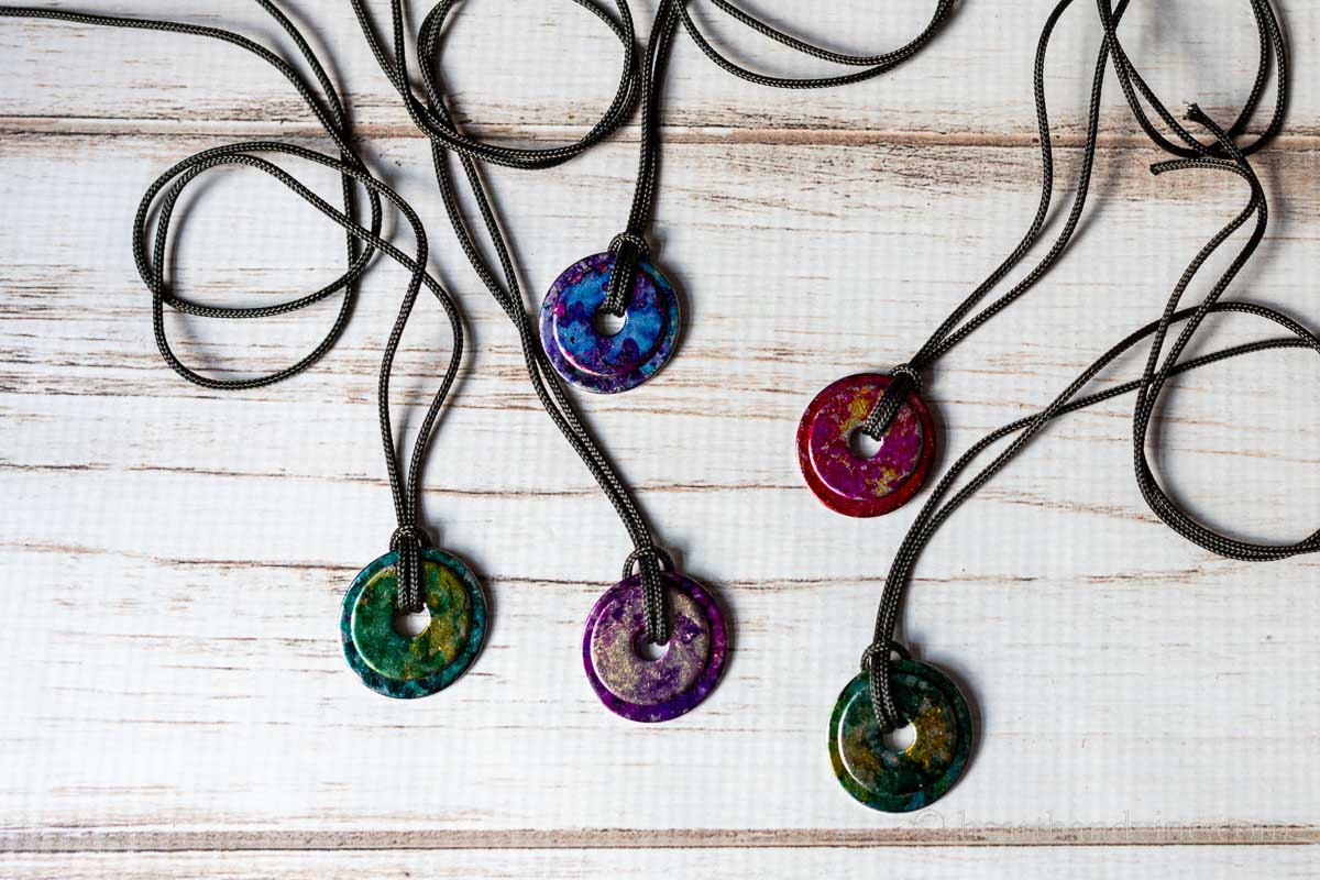 Five different colored alcohol ink painted metal washers attached to cording to create necklaces.