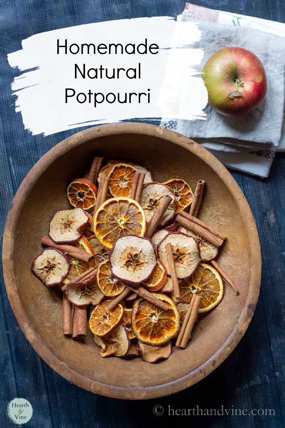 Wooden bowl filled with dried apple and orange slices and cinnamon sticks.