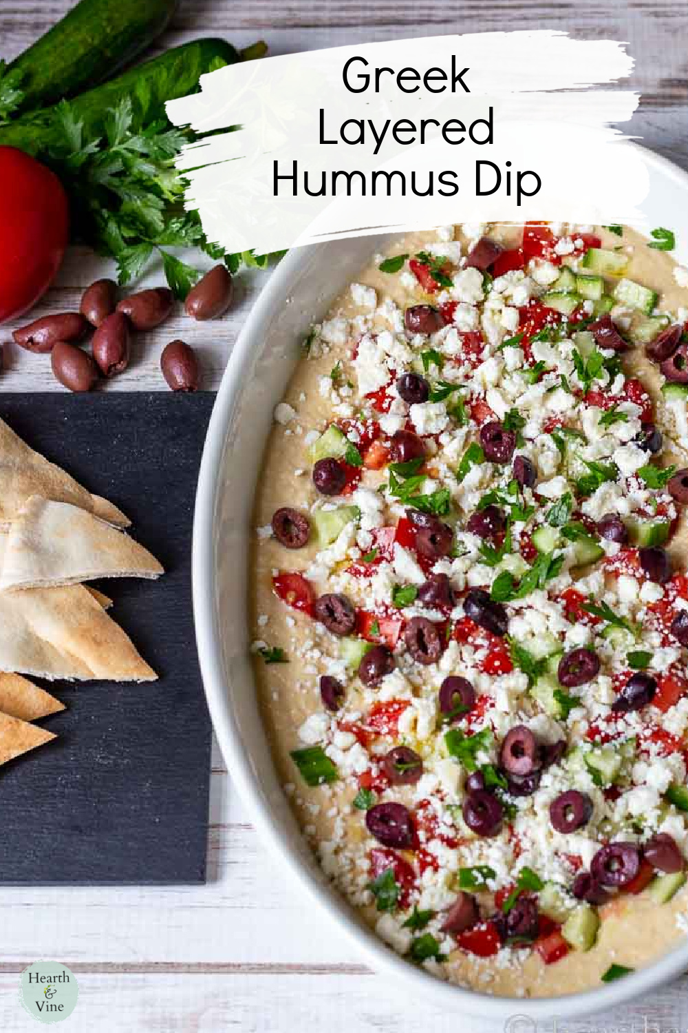 Oval platter with Greek Layered Hummus dip, and pita wedges on the side.