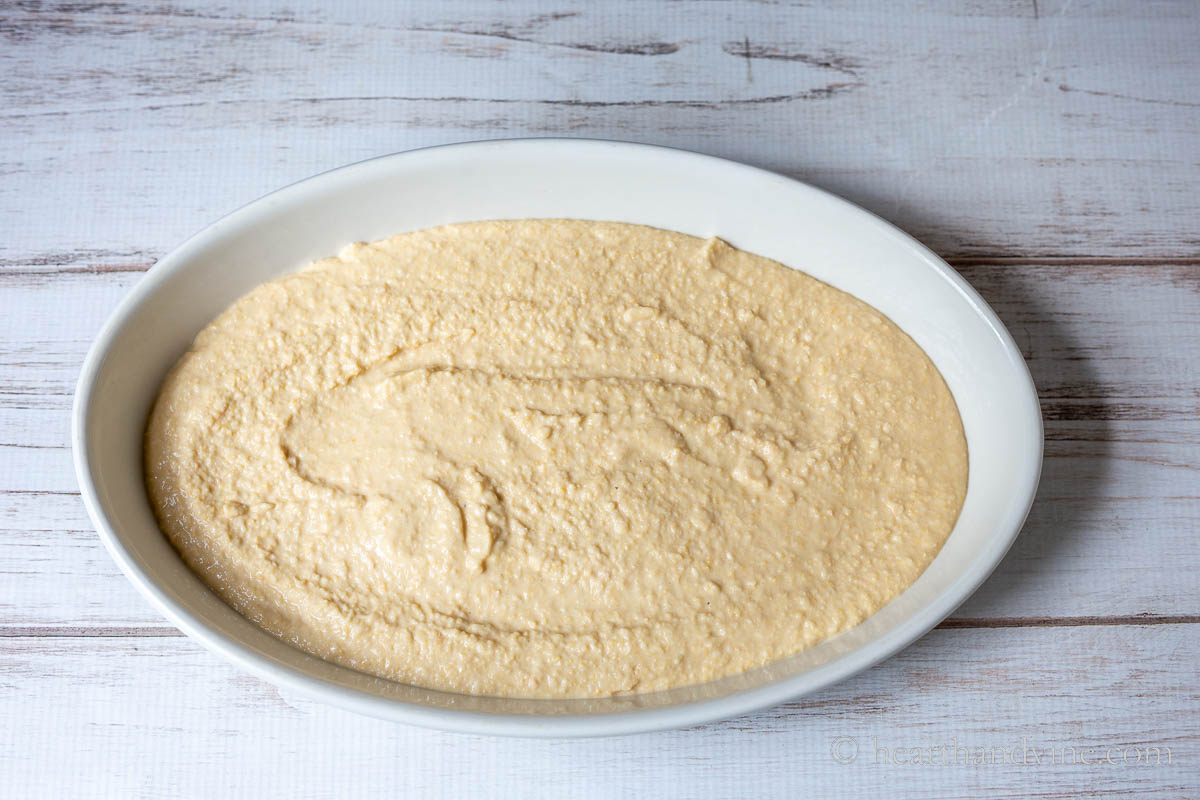 A large oval serving dish with a layer of freshly made hummus.