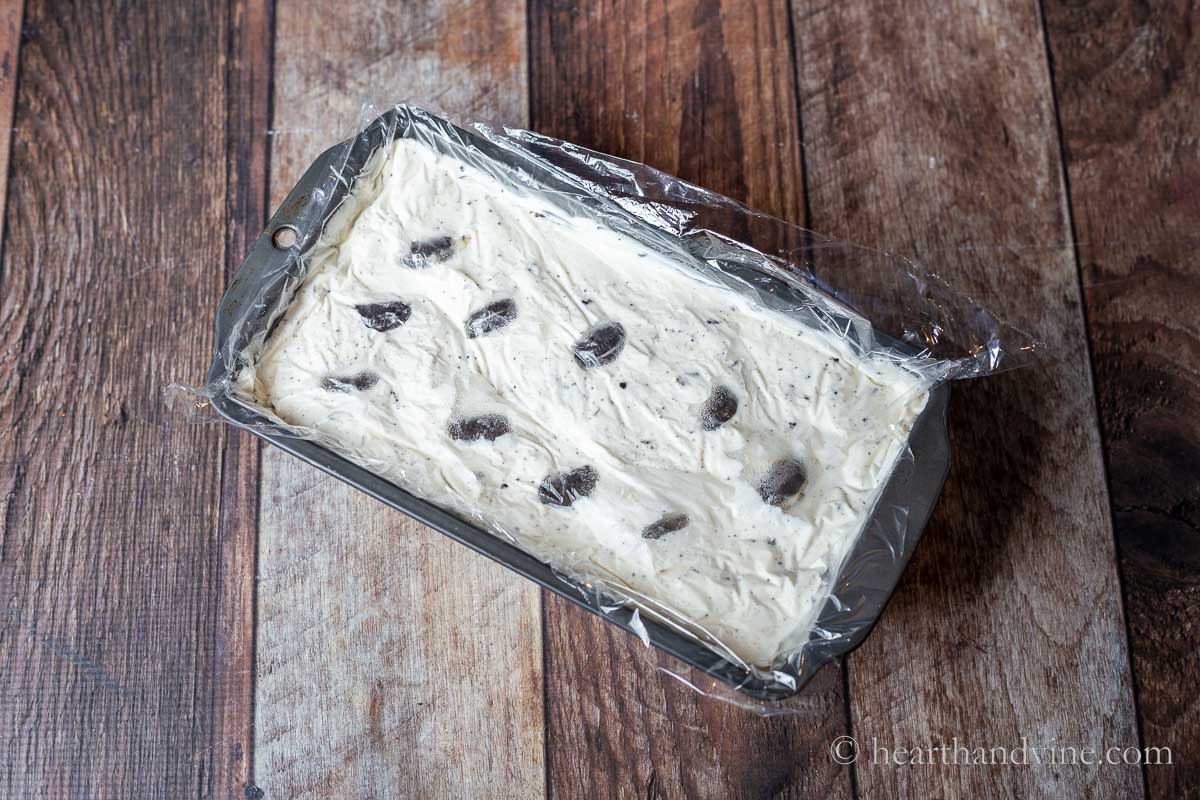 Oreo ice cream in a loaf pan with plastic wrap on top.