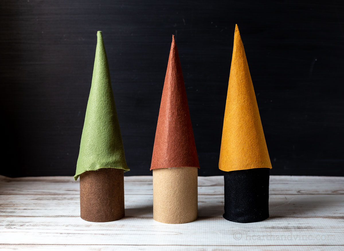 Pillar candles covered with felt topped with tall cones of felts in olive, sienna and gold.