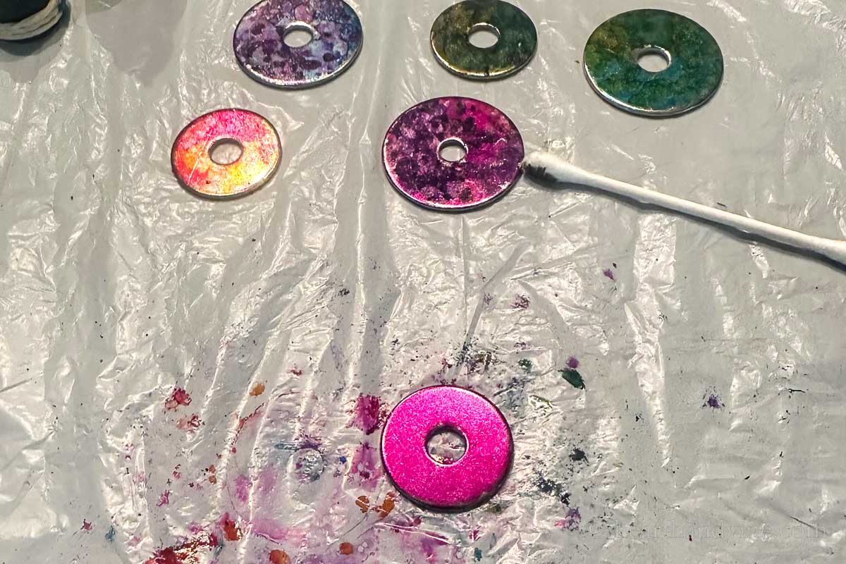 A metal washer covered in pink alcohol ink below several other painted metal washers.