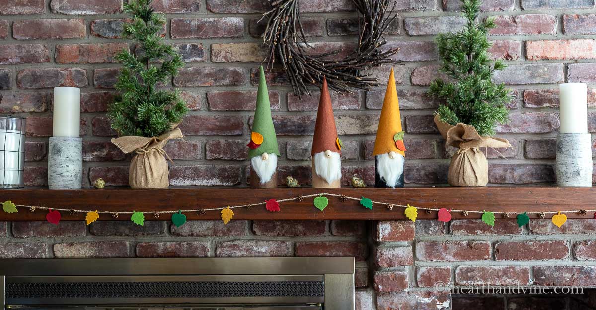 Fall decorated mantel with felt fall leaf garland, gnomes, candles and trees.