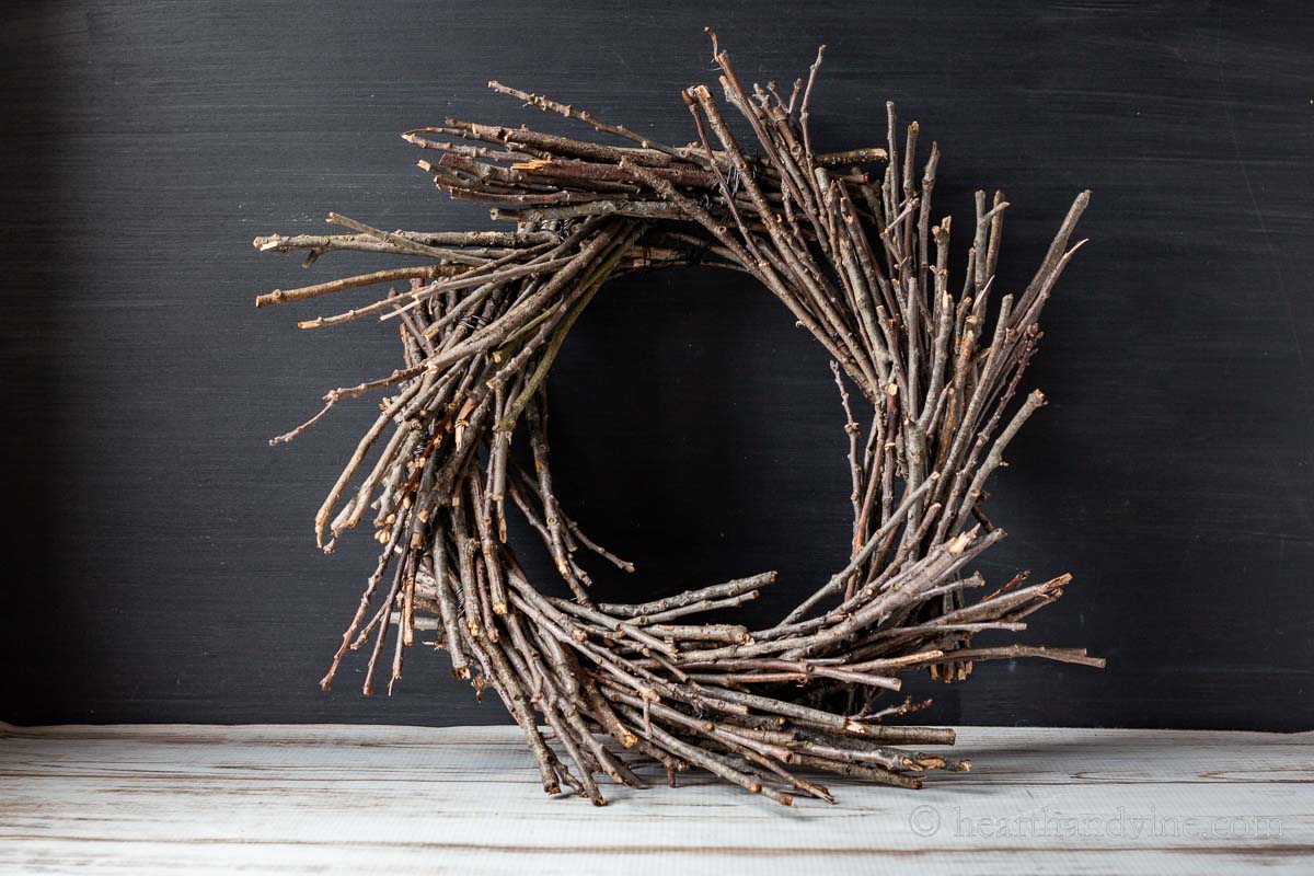 A natural twig wreath on a table with a black backdrop.