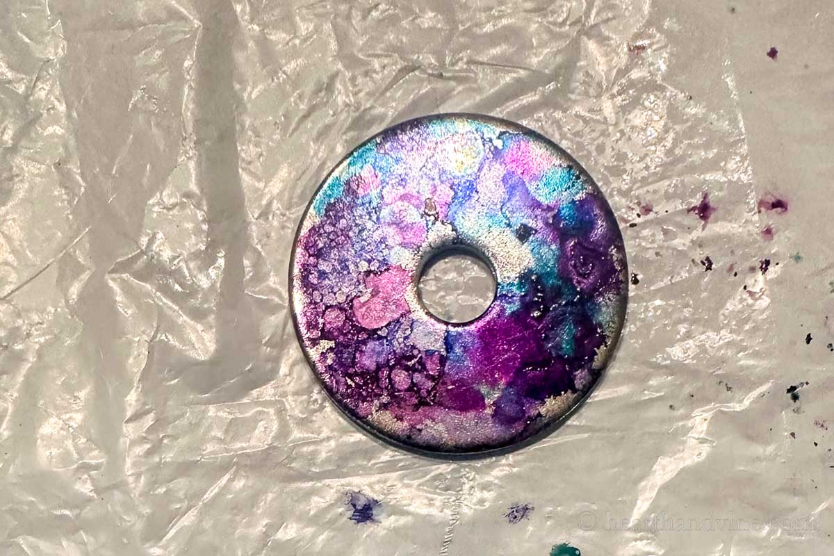 A metal washer with alcohol ink that has been sprayed with isopropyl alcohol.