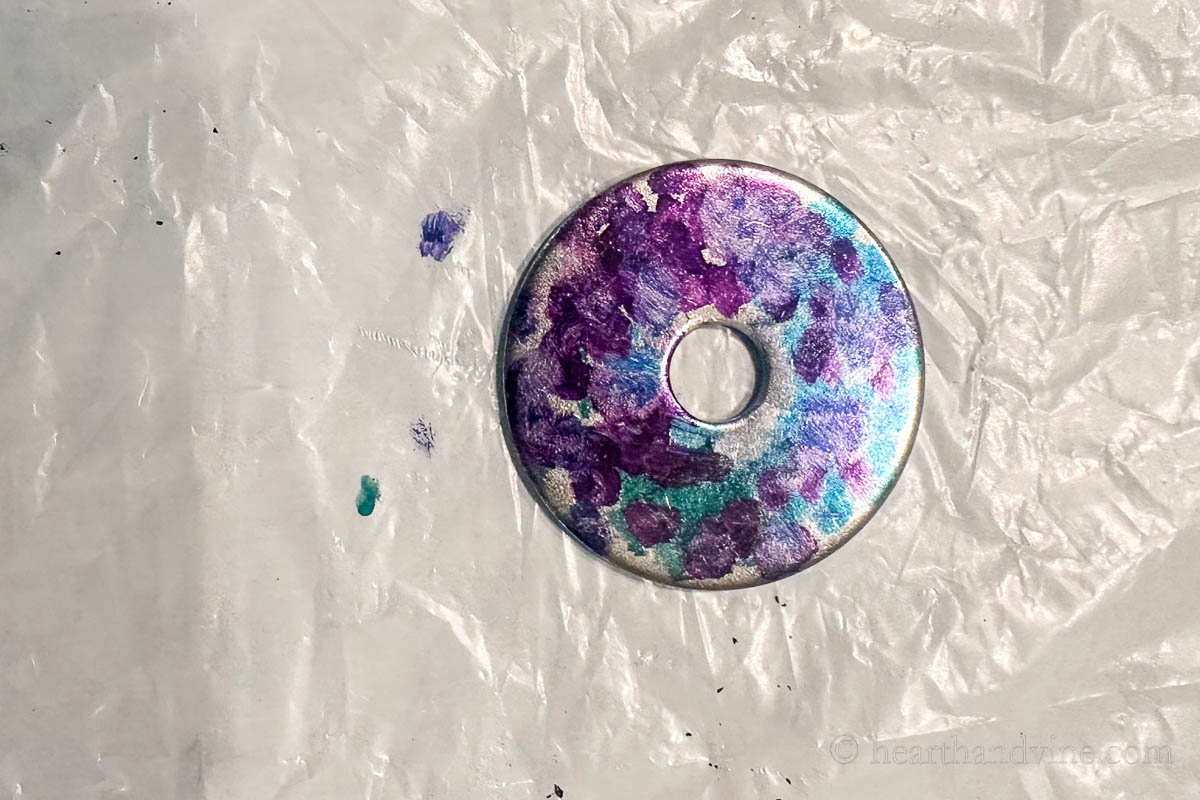 A metal washer with purple and blue alcohol ink dabbed around.