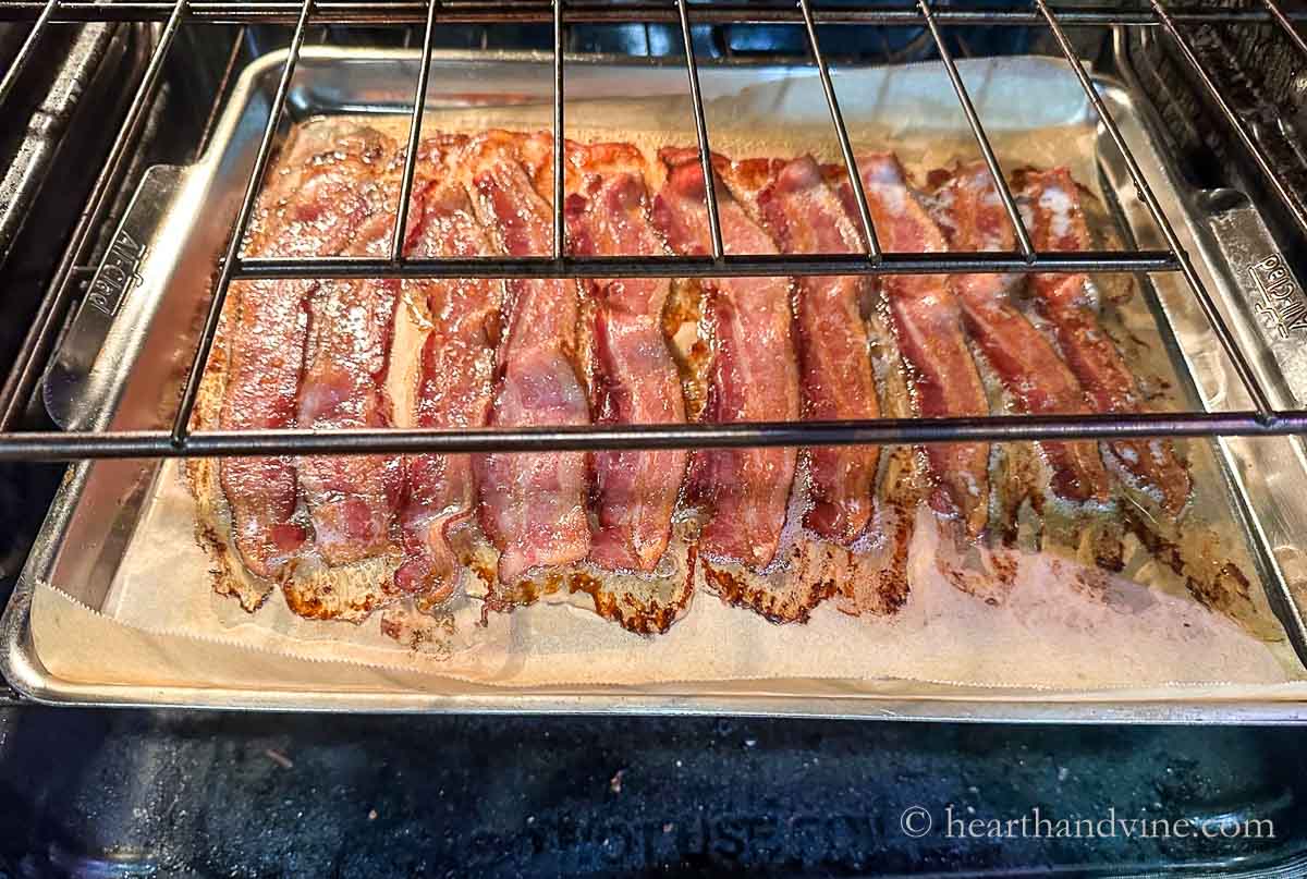 Bacon cooking in the oven on parchment and a jelly roll pan.