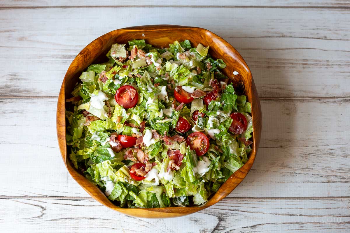 Bacon, lettuce and tomato salad tossed with creamy blue cheese dressing in a large wooden salad bowl.