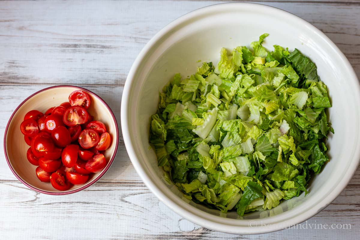 A small bowl of halved cherry tomatoes and another larger bowl of chopped romaine lettuce.