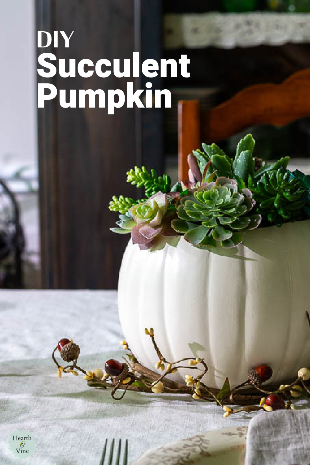 A succulent pumpkin centerpiece with an acorn garland around the bottom on a Thanksgiving table.