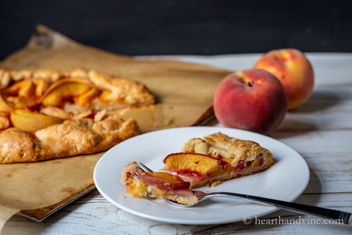 A slice of the peach crostata on a small plate next to a couple of fresh peaches and the rest of the crostata.