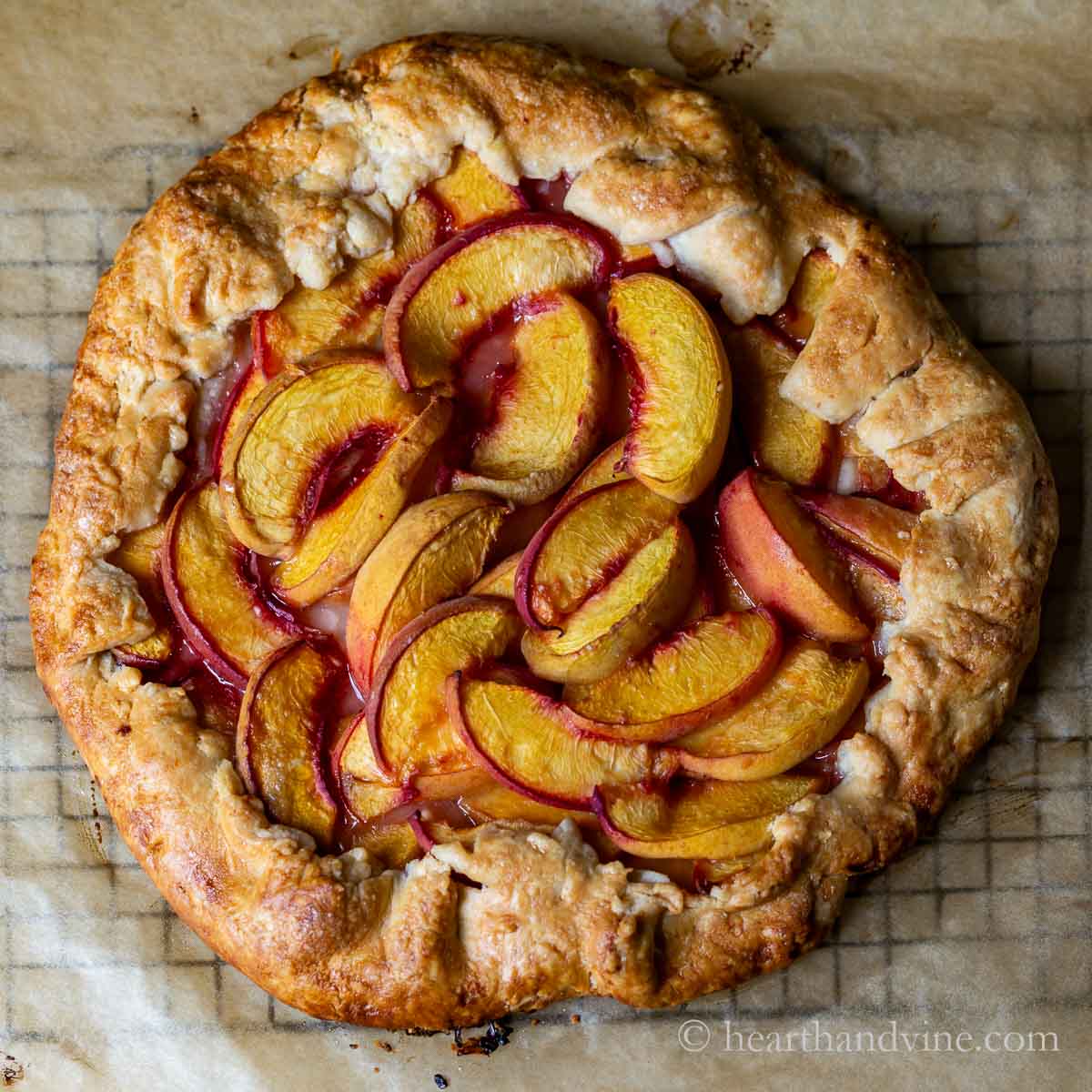 Rustic baked peach crostata on parchment paper on a cooling rack.