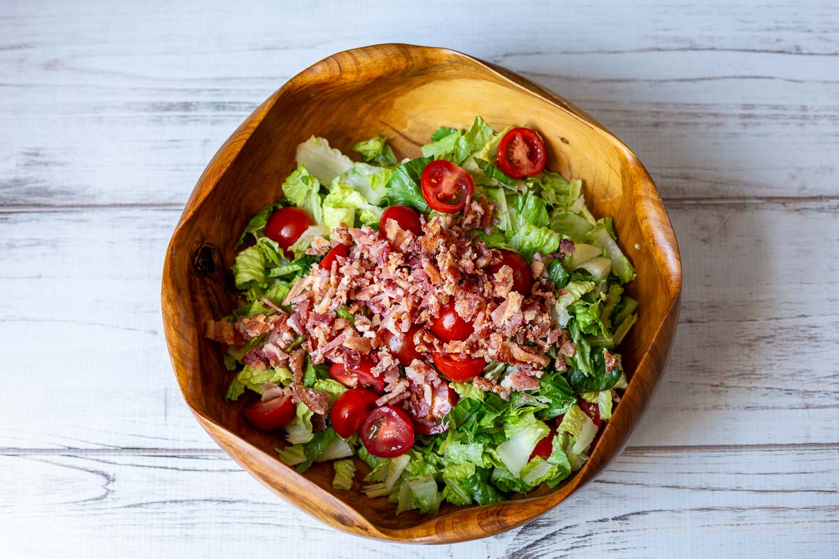 A large wooden salad bowl with chopped romaine lettuce, cherry tomatoes and chopped bacon.
