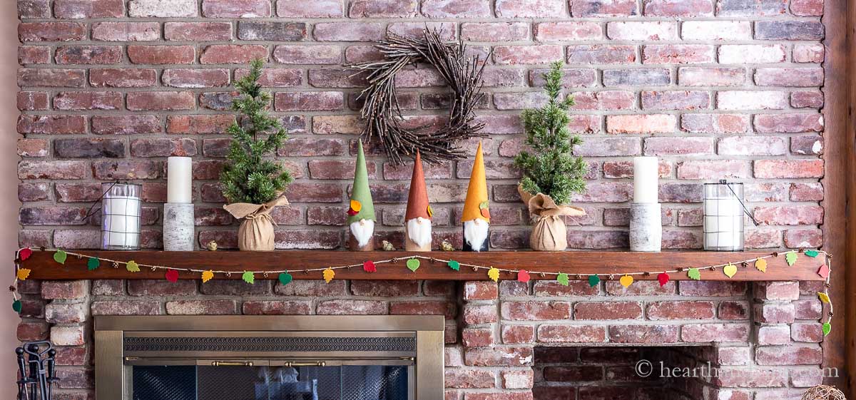 Fall mantel with twig wreath, fall gnomes, felt garland, and candles.