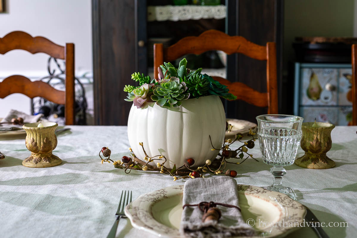 A foam white pumpkin with succulent in the top as a centerpiece for a fall or Thanksgiving table.
