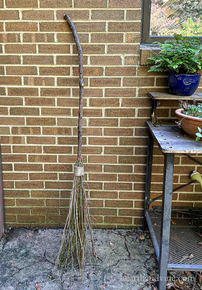 Handmade witches broom leaning against a brick wall.