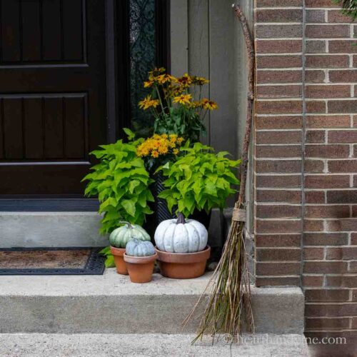 Handmade witches broom leaning against the brick of a front porch.