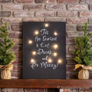 Black chalkboard sign with lights saying Tis the season to eat, drink and be merry.