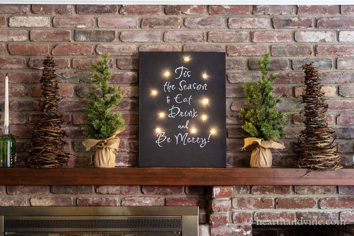 The DIY lighted sign on a mantel with trees and candles.