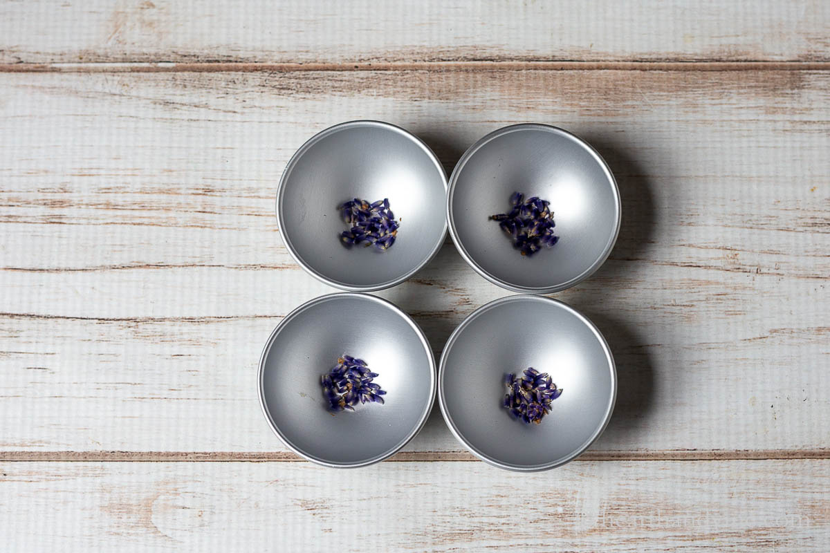 Four metal bath bomb molds with dried lavender buds in the bottom.