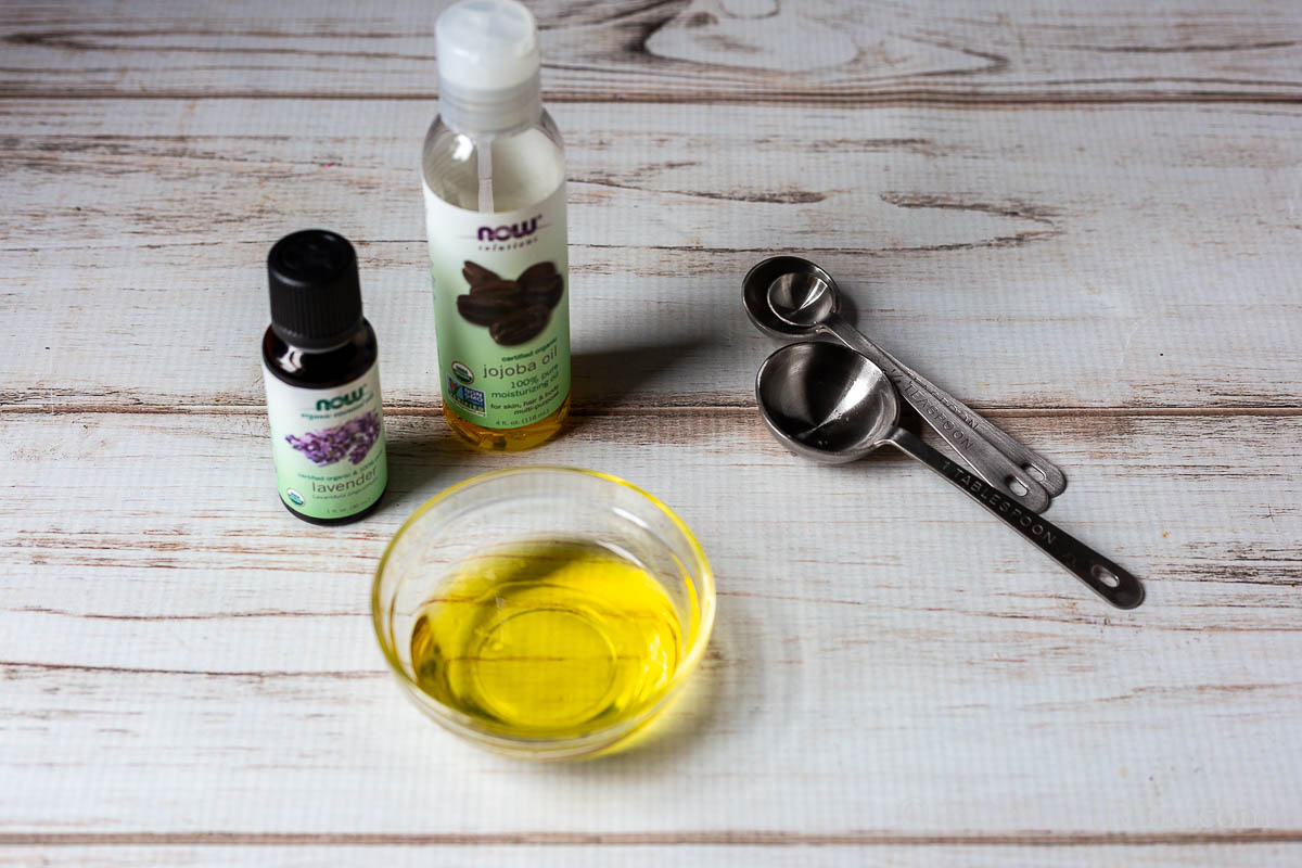 Essential oil of lavender, jojoba oil, measuring spoons and a small bowl of the oils.