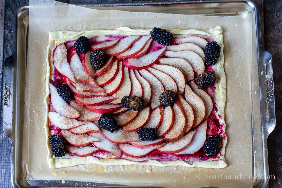 Fresh pears thinly sliced and arranged on a sheet of puff pastry with a few blackberries on top dusted with cinnamon.