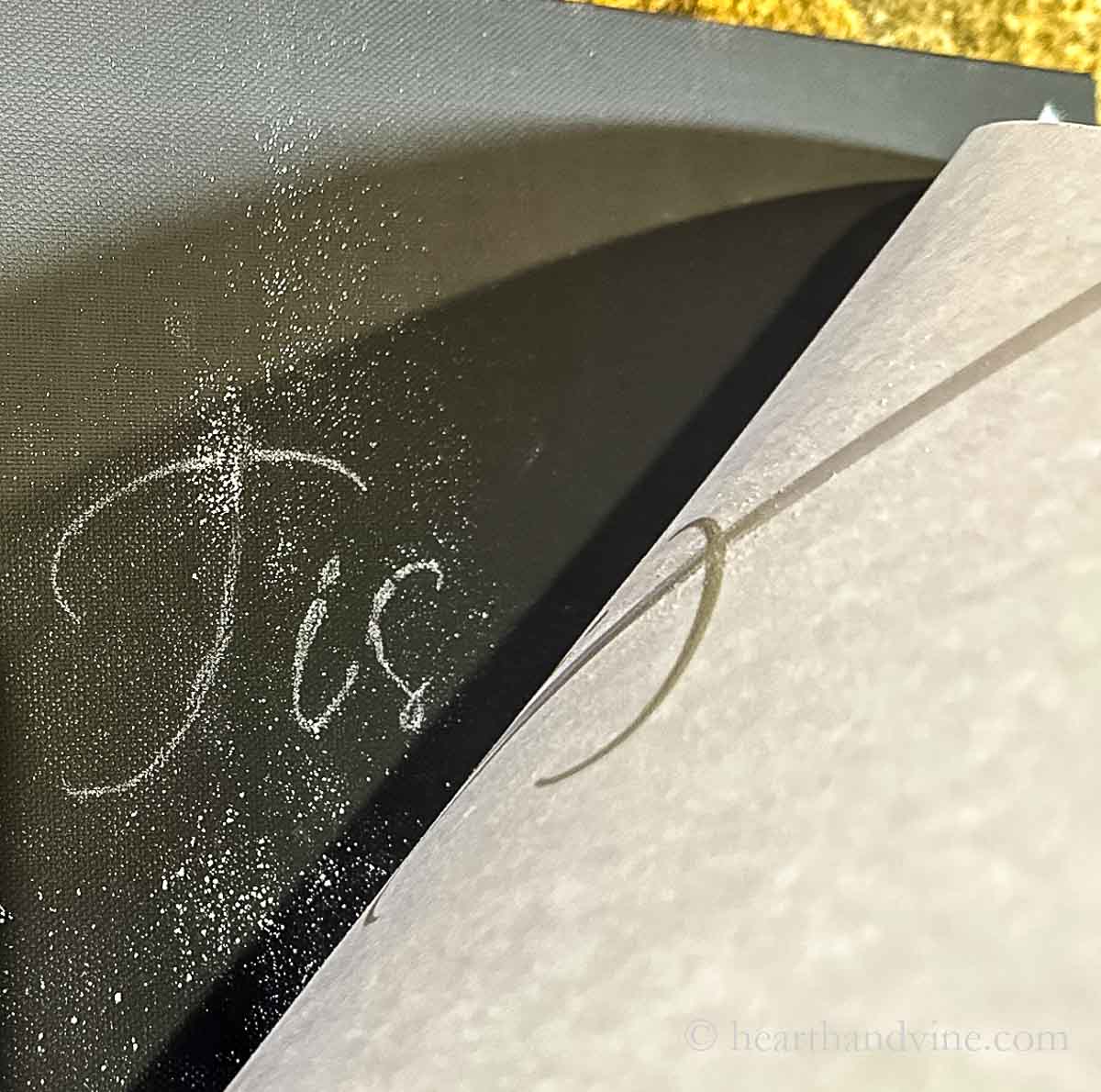 Paper lifted up to show the chalk transfer underneath showing the word "Tis."
