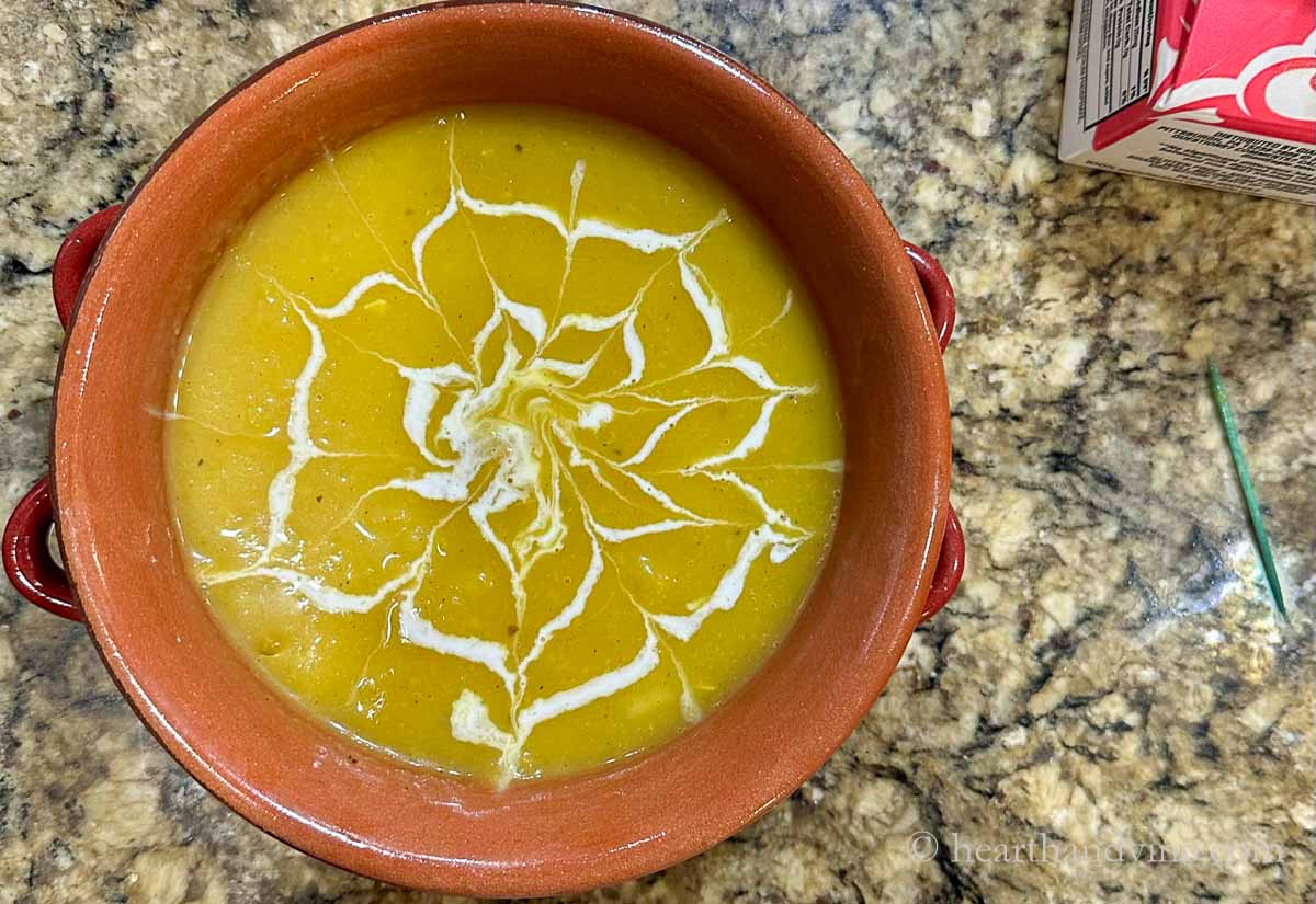 A bowl of delicata soup with a spider web design using a toothpick.