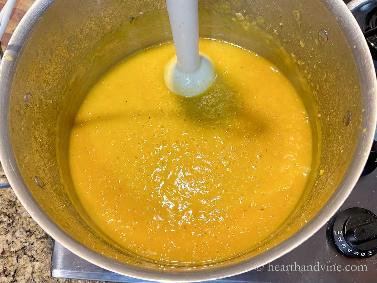 An immersion blender in large pot creaming all the vegetables, spices and broth.